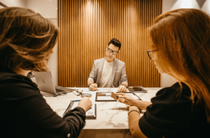 Serious HR professional filling out paperwork on marble desk between the heads of two candidates seated on other side