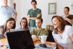 7 team members leaning over to look at an opened laptop, engaged in a webinar