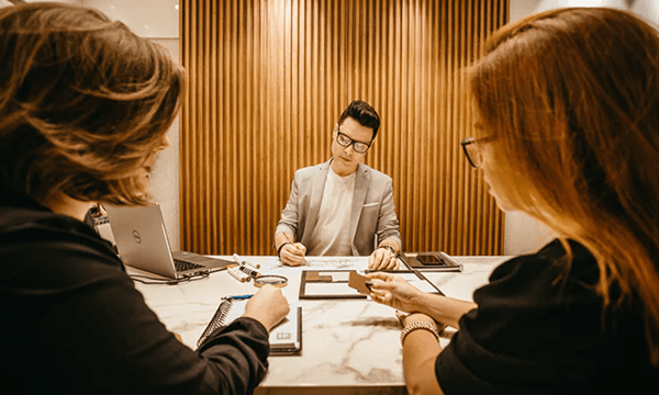 tile-Serious HR professional filling out paperwork on marble desk between the heads of two candidates seated on other side