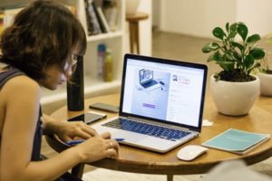 Side view of woman diligently working on computer at table, with smartphone, mouse and notebook