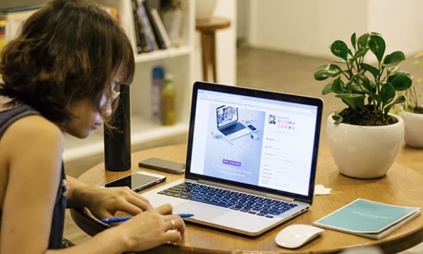 tile-Side view of woman diligently working on computer at table, with smartphone, mouse and notebook