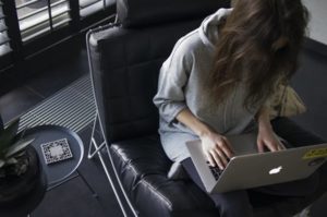 Woman with hair covering face working diligently on laptop, seated in leather chair in dark and posh lobby space