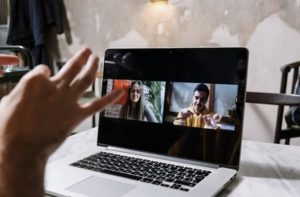 Close up view of open laptop on desk at home with two participants in Gallery View, and hand gesticulating in foreground