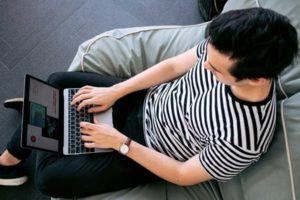 View looking down on a man sitting comfortably in bean bag chair, typing and engaging with laptop