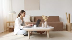 Young woman working on laptop at home, seated on floor at a low table, in stylish living room