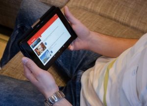 Close up view of lower half of man sitting on couch, using YouTube on a tablet device