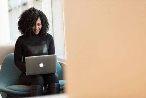 On left side, view of woman working on laptop in stylish chair seen from around the corner of a peach-colored wall on right side