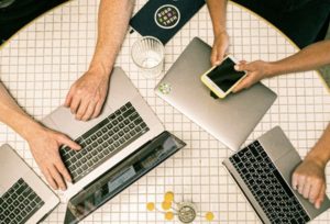 Over head view of three sets of arms using laptops on tiled, grid-like round table