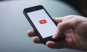 tile-Close of up a hand holding a smartphone with YouTube app visible onscreen