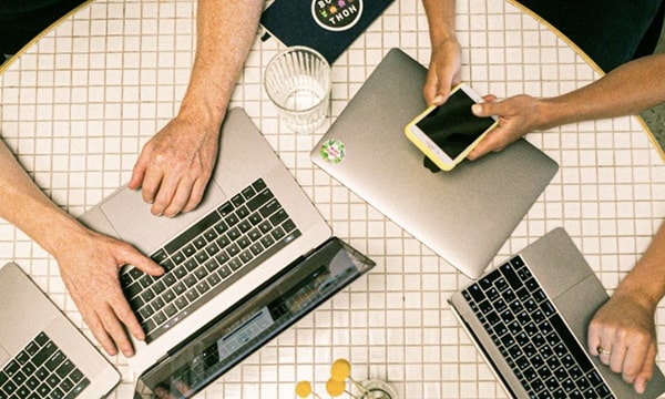 tile-Over head view of three sets of arms using laptops on tiled, grid-like round table