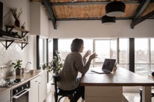 Side view of woman sitting at kitchen island chatting and gesticulating into laptop
