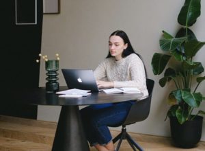 Woman diligently working on laptop in contemporary-styled workspace with stylish touches, and plant in background