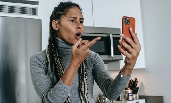 Woman in kitchen pointing and talking into smartphone held up to her face