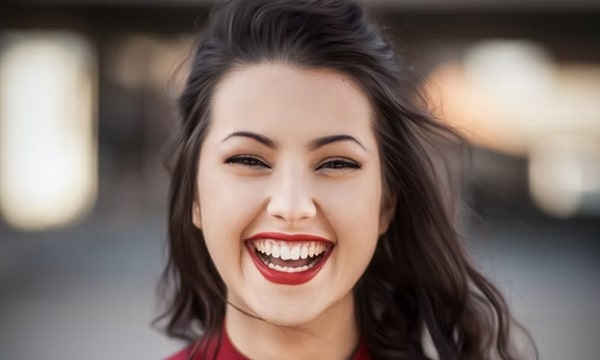 Happy, beautiful young woman facing camera with long brown hair and a wide smile wearing a dark red mock turtleneck top